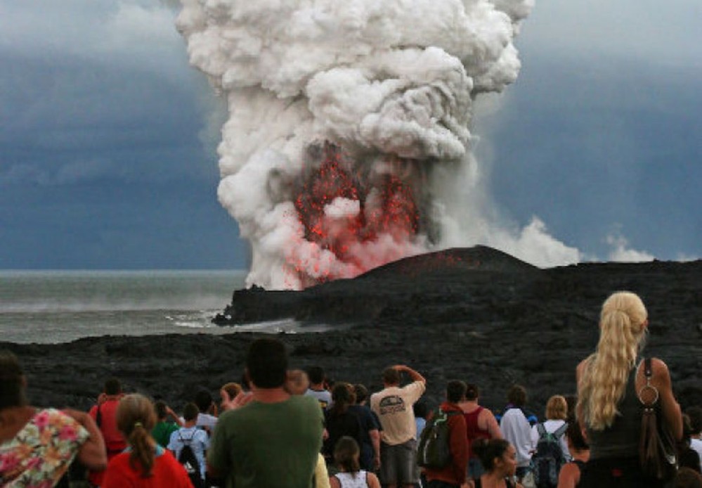 turistas frente a un volcán en erupción, de día